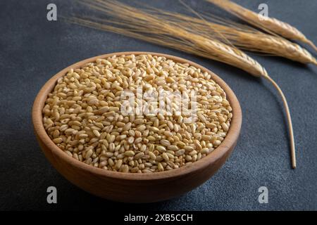 Wheat grains in wooden bowl and ears on black background Stock Photo