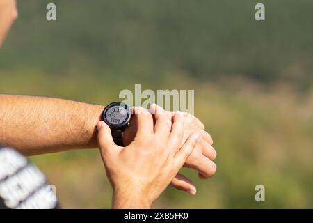 Runner on mountain forest trail checking looking at sport watch smartwatch cross country runner hiker checking performance distance heart rate pulse Stock Photo