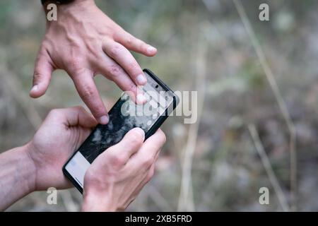 close up of a man using gps navigation app on his smartphone in nature and other guy pointing at the screen with his finger, using phone as navigation Stock Photo