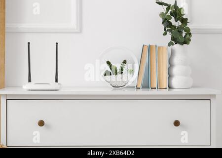 Modern wi-fi router with books and florarium on commode in room Stock Photo