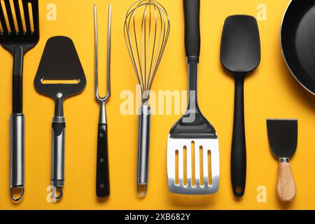 Different spatulas and other kitchen utensils on orange background, flat lay Stock Photo