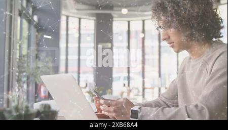 Young biracial man using smartphone while working on laptop in modern cafe Stock Photo