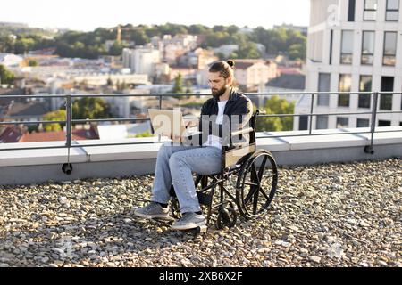 Man in wheelchair working on laptop in outdoor urban setting Stock Photo