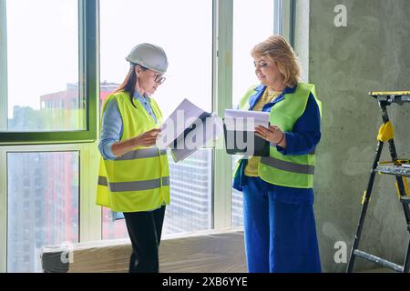 Two female industrial workers with technical plan at construction site Stock Photo