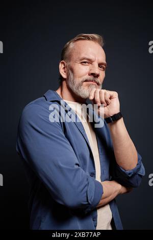 Vertical fashion portrait of bearded senior man looking at camera with confidence while posing in studio Stock Photo