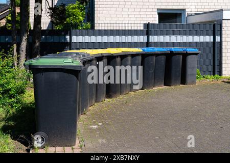 Plastic bins for separate waste collection are lined along the fence of a residential building. Bins caps in different colors. Stock Photo