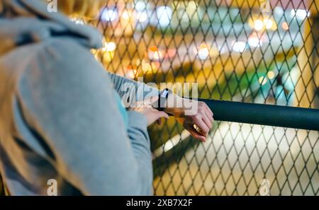 Close up of unrecognizable female hand touching digital wrist band screen to check daily step counter after walking at night on town. Woman athlete lo Stock Photo