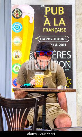 Man seated at cafe / pub table with glass of beer reading from smartphone - Tours, Indre-et-Loire (37), France. Stock Photo