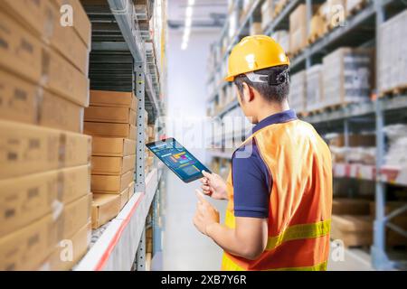 Asian worker or engineer in warehouse with stack of cardboard boxes Stock Photo