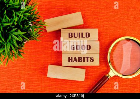 build good habits inspirational writing on wooden blocks with a flower and a magnifying glass in the composition . Beautiful orange background Stock Photo