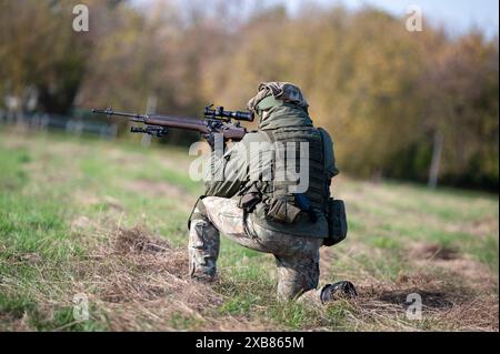 A man in camouflage crouches holding a rifle Stock Photo