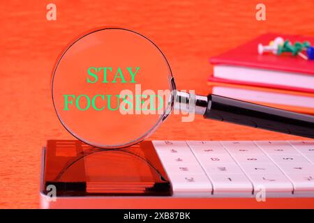 Concept words Stay focused written through a magnifying glass on a calculator on an orange background Stock Photo