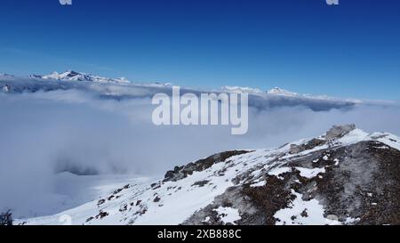 A partially snow-covered mountain peak above clouds Stock Photo