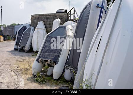 Upturned inflatable dinghies and small boats on concrete dock, ready for repair or storage by marina boat access. Stock Photo