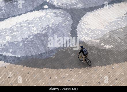 Munich, Germany. 11th June, 2024. A man cycles across a cobbled square in the Werksviertel district of the Bavarian capital. Credit: Peter Kneffel/dpa/Alamy Live News Stock Photo