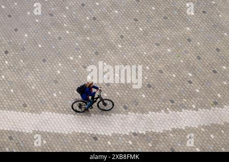 Munich, Germany. 11th June, 2024. A woman cycles across a cobbled square in the Werksviertel district of the Bavarian capital. Credit: Peter Kneffel/dpa/Alamy Live News Stock Photo