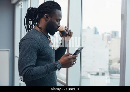 An African Man with dreadlocks is drinking coffee while looking at his cell phone reading messages. concept of technology and digital connections, as Stock Photo