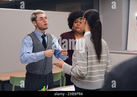 A Man and tow Women are standing in a meeting room, the man is explaining something to the women.They are talking to each, they are wearing business c Stock Photo