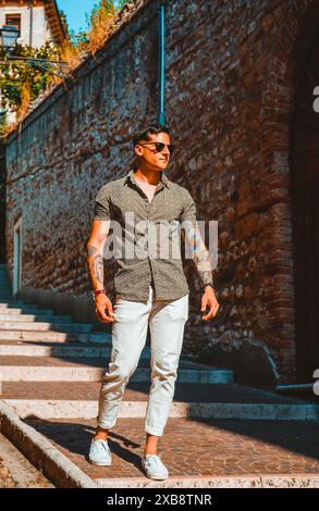 Stylish young man in sunglasses and dress shirt strolling in urban setting Stock Photo