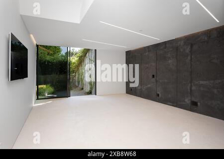 Minimalist room with concrete walls, white floors, and wall-mounted TV Stock Photo
