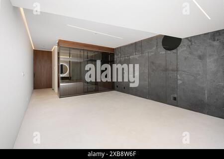 A vacant bedroom with concrete walls and a ceiling fan Stock Photo