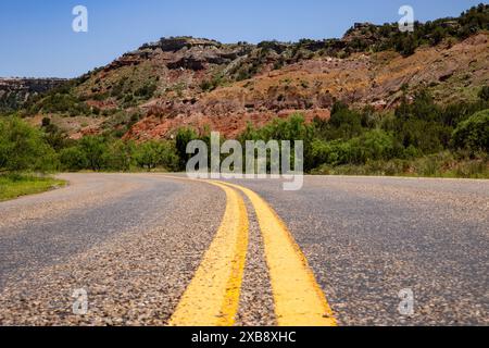 A deserted road winds through rocky hillsides with grass Stock Photo