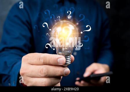 Businessman holding glowing lightbulb and question mark with copy space for creative thinking idea and problem solving concept. Stock Photo