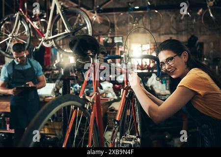Happy woman, portrait and bicycle mechanic with inspection, fix or maintenance at repair shop. Young female person, cycling technician or engineer Stock Photo