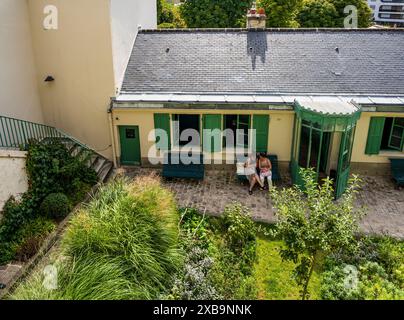 A couple sitting on a bench and relaxing in front of Maison de Balzac surrounded by vegetation, in Passy quarter, Paris, France Stock Photo