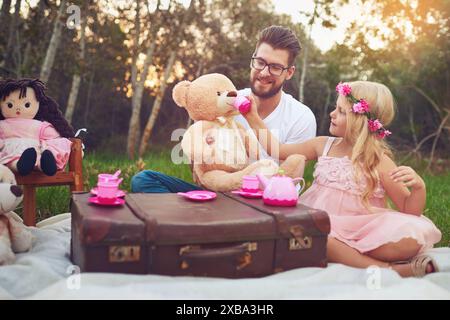 Father, tea party and girl kid in garden for nature picnic with toys, teddy bear drink and suitcase for table. Daughter, dad and memory together for Stock Photo