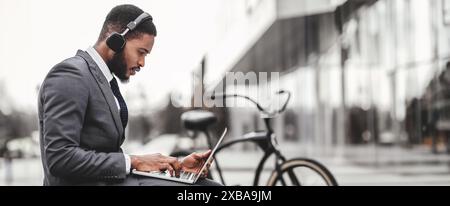 African American businessman using headphones and laptop outdoors Stock Photo