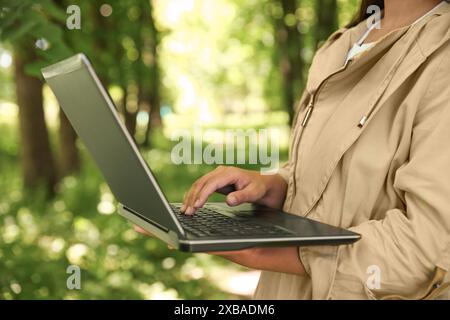 Forester with laptop examining plants in forest, closeup Stock Photo