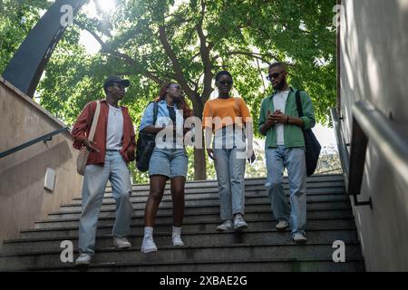 Interested black four girls and guys students down to stairs to underpass chatting going in college. Stock Photo
