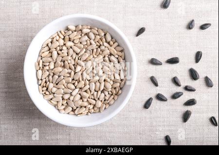 Hulled sunflower seeds in a white bowl on linen fabric. Fruits of the oilseed Helianthus Annuus, the common sunflower. Stock Photo