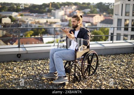 Young man using smartphone while sitting in wheelchair on rooftop Stock Photo