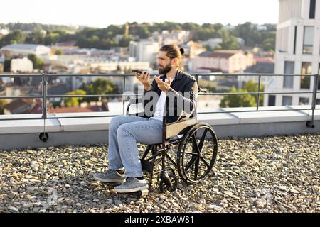 Man in wheelchair using smartphone on rooftop with city view Stock Photo