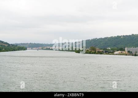 A wide shot of the Isere River flowing through the city of Grenoble, France, with a view of the surrounding mountains in the background on a cloudy da Stock Photo