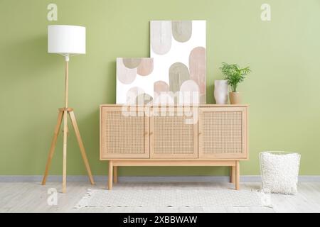 Wooden chest of drawers, lamp and beautiful pictures on green wall in room Stock Photo