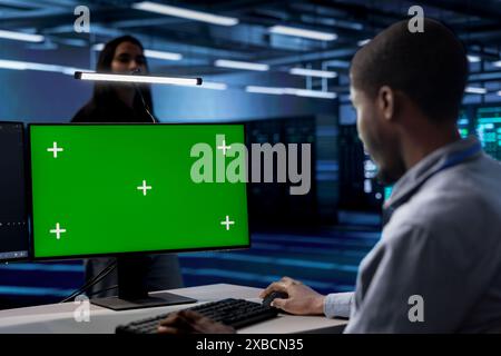 Technician using green screen desktop PC to oversee servers used for managing databases. African american man working on mockup computer monitor in data center storing information Stock Photo