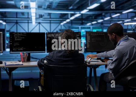 Person with paraplegia working in inclusive workplace typing data on PC, doing needed adjustments in supercomputers server hub housing advanced data storage infrastructure Stock Photo