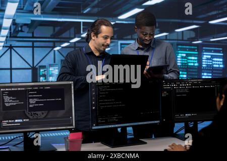 Coworkers in data center using laptop and tablet to find firewall misconfigurations affecting servers. Colleagues in server room checking systems bottlenecks leading to sluggish data transfer rates Stock Photo