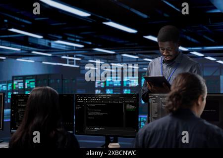 Multiethnic team in server room checking recovery plan and monitoring energy consumption. Diverse group of employees in data center location doing routine disk checks across components Stock Photo