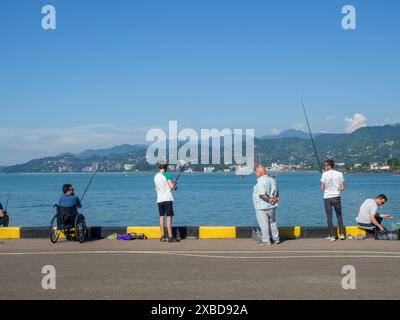 Batumi, Georgia. 04.06.2024 Fishermen on the Batumi embankment. Fishing in the port. Fishing rods on the pier. Hobbies of men. Wheelchair Stock Photo