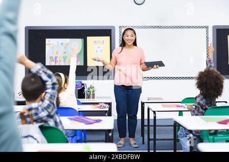 In school, female teacher engaging with diverse students raising hands ...