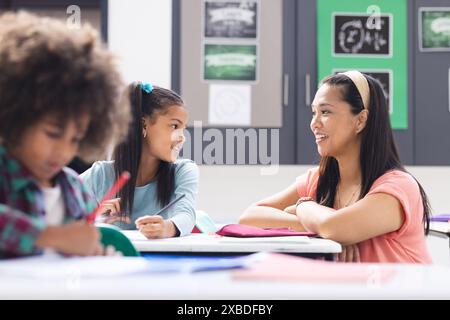 Biracial female teacher interacting with two students in classroom Stock Photo