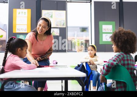 A biracial teacher helping group of biracial students in classroom Stock Photo