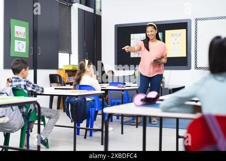 Biracial female teacher engaging with diverse students in classroom setting Stock Photo