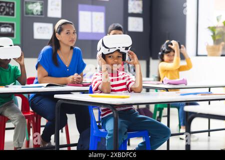 Biracial female teacher and children using VR sets in classroom Stock Photo