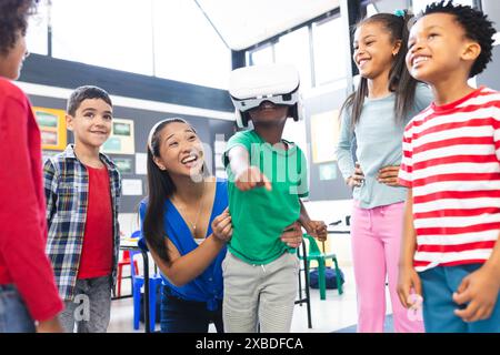 A biracial teacher guiding group of diverse students using VR headset Stock Photo