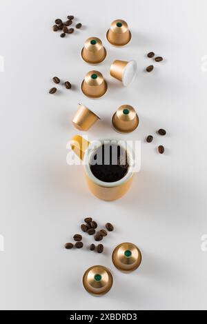 Yellow coffee cup with golden coffee capsules and beans on a white background. Stock Photo